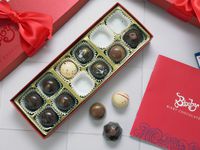 box of bixby chocolates with lid off and three bonbons on a white tile surface