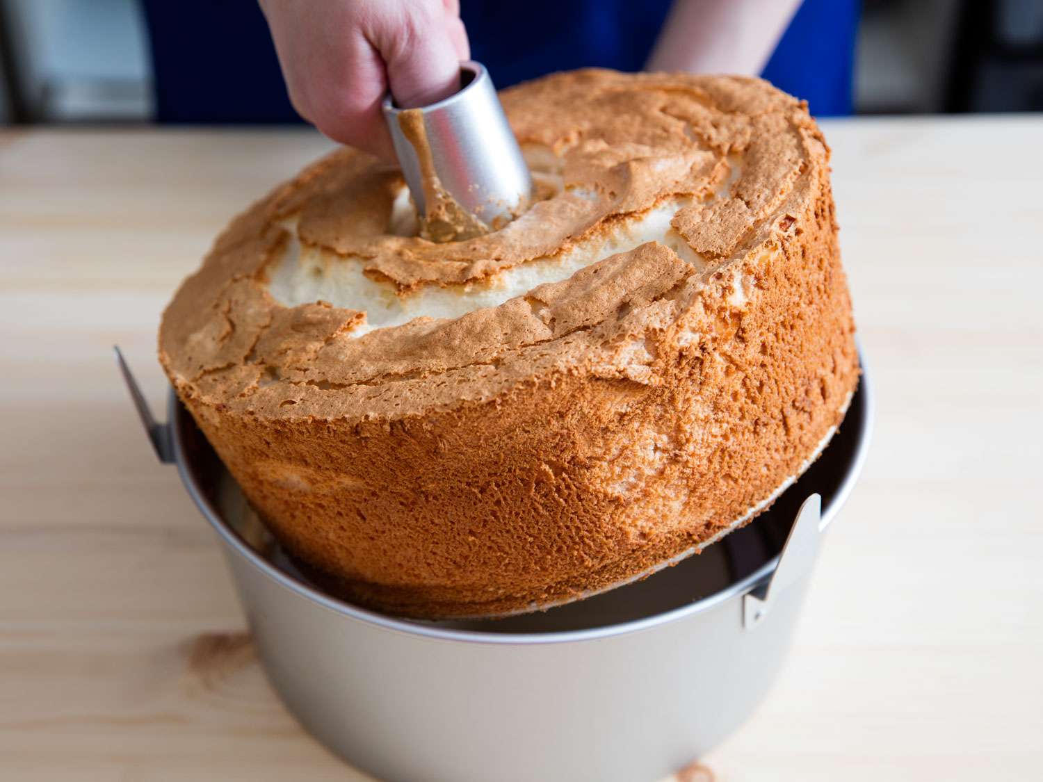 Cooled angel food cake being lifted out of tube pan.