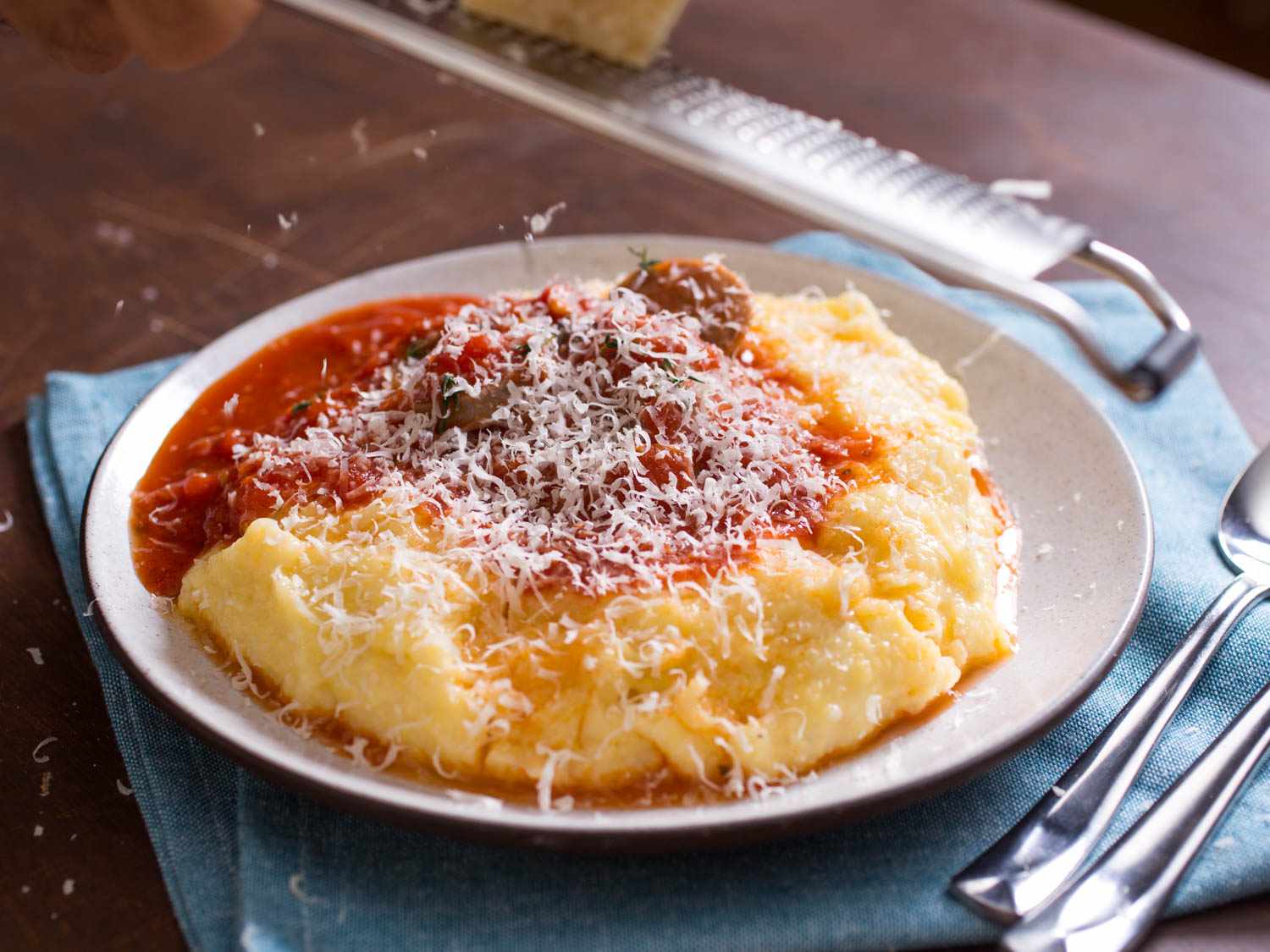 Polenta on a plate topped with tomato sauce, sausage, and cheese.