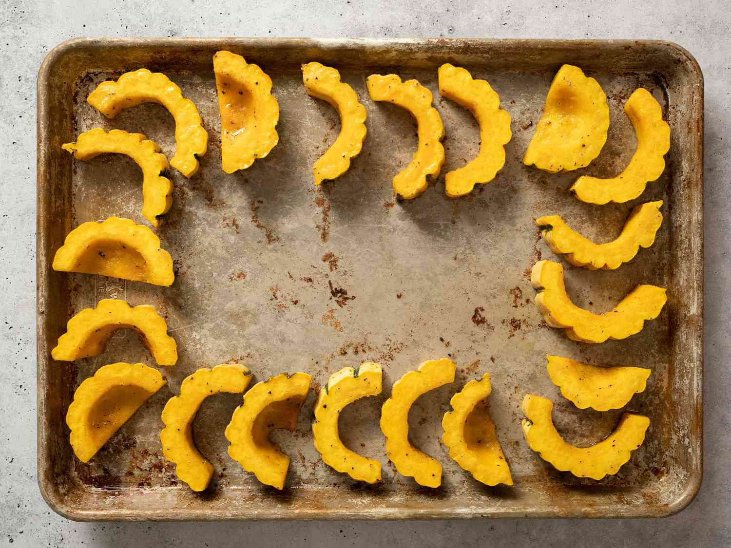 Delicata squash slices arranged on perimeter of a rimmed baking sheet.