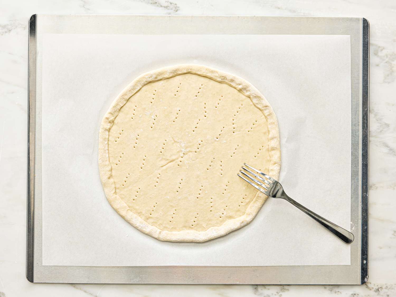 A round sheet of pastry dough on parchment paper with a fork placed on top on a baking sheet surface