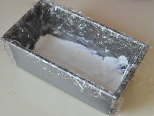 A loaf pan lined with plastic wrap, with whipped cream on the bottom.