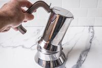 A hand holding a metal stovetop coffee maker by its handle