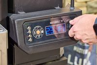 A person turns a dial on the Masterbuilt Gravity Series 1150 Digital Charcoal Grill and Smoker