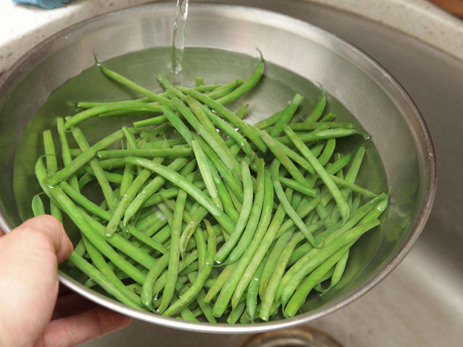 Running just-blanched green beans under cold water in a bowl.