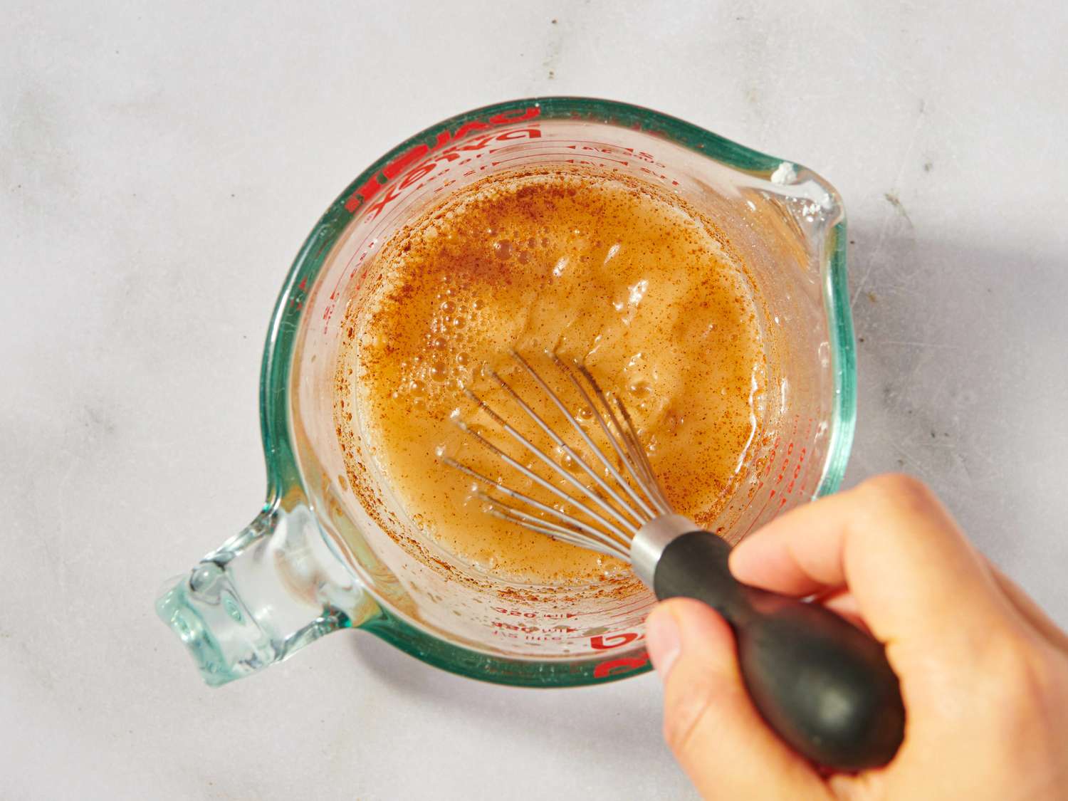 A hand whisking a mixture in a measuring cup