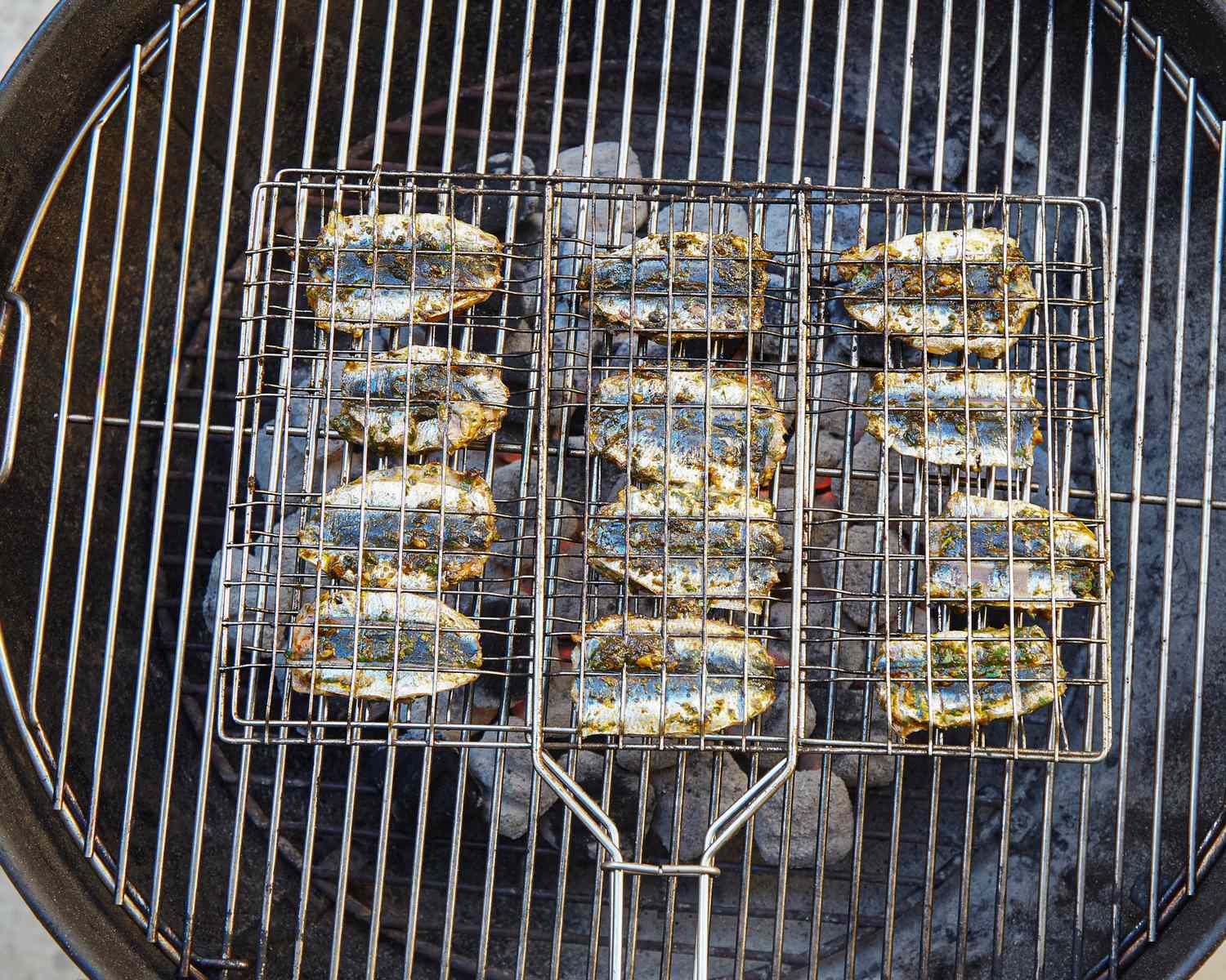 Sardines being grilled on a rack over charcoal