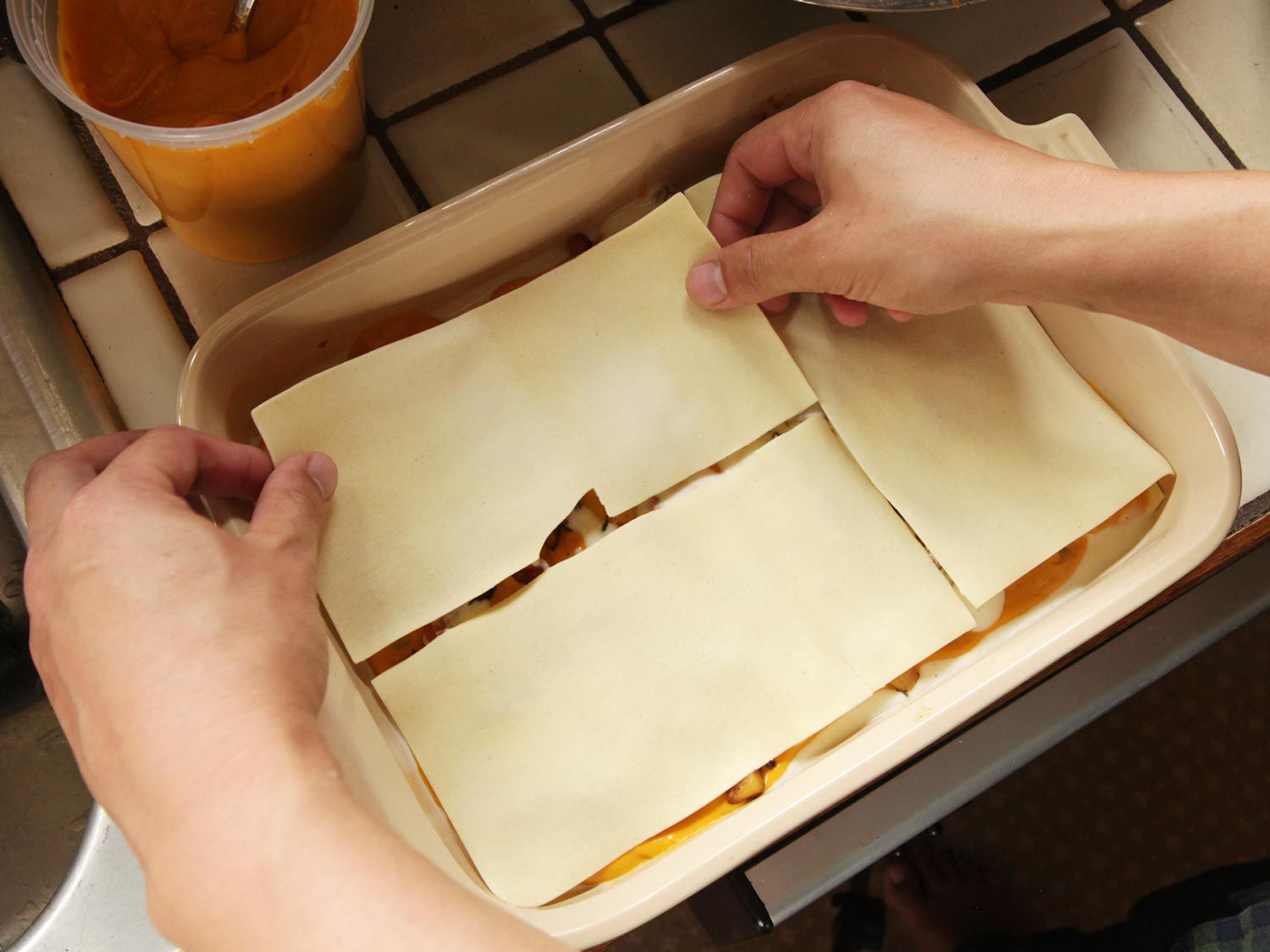 Layering pasta sheets over fillings in a baking dish.