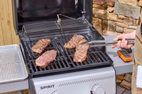 A hand using tongs to lift steak on the Weber Spirit E-210 Gas Grill