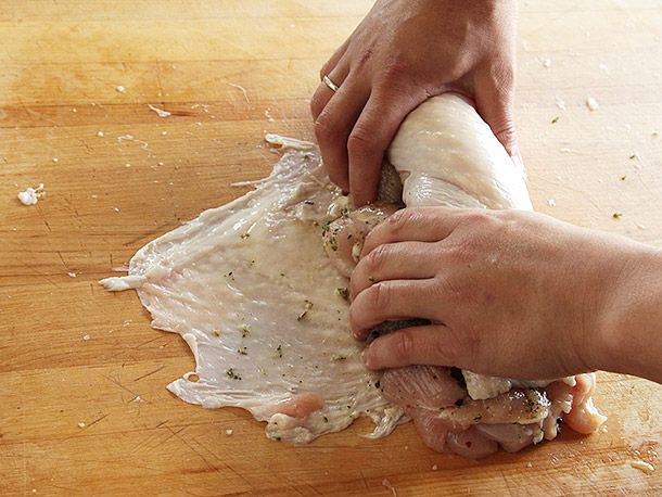 Tucking turkey breast meat under the skin as hands are rolling the seasoned breast meat in the skin for turkey porchetta (turchetta).