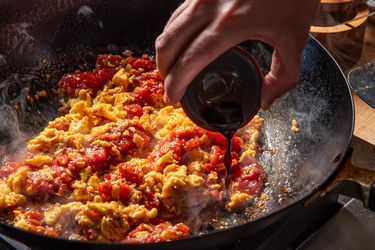 Ingredients being cooked in a pan with a liquid being poured in by hand