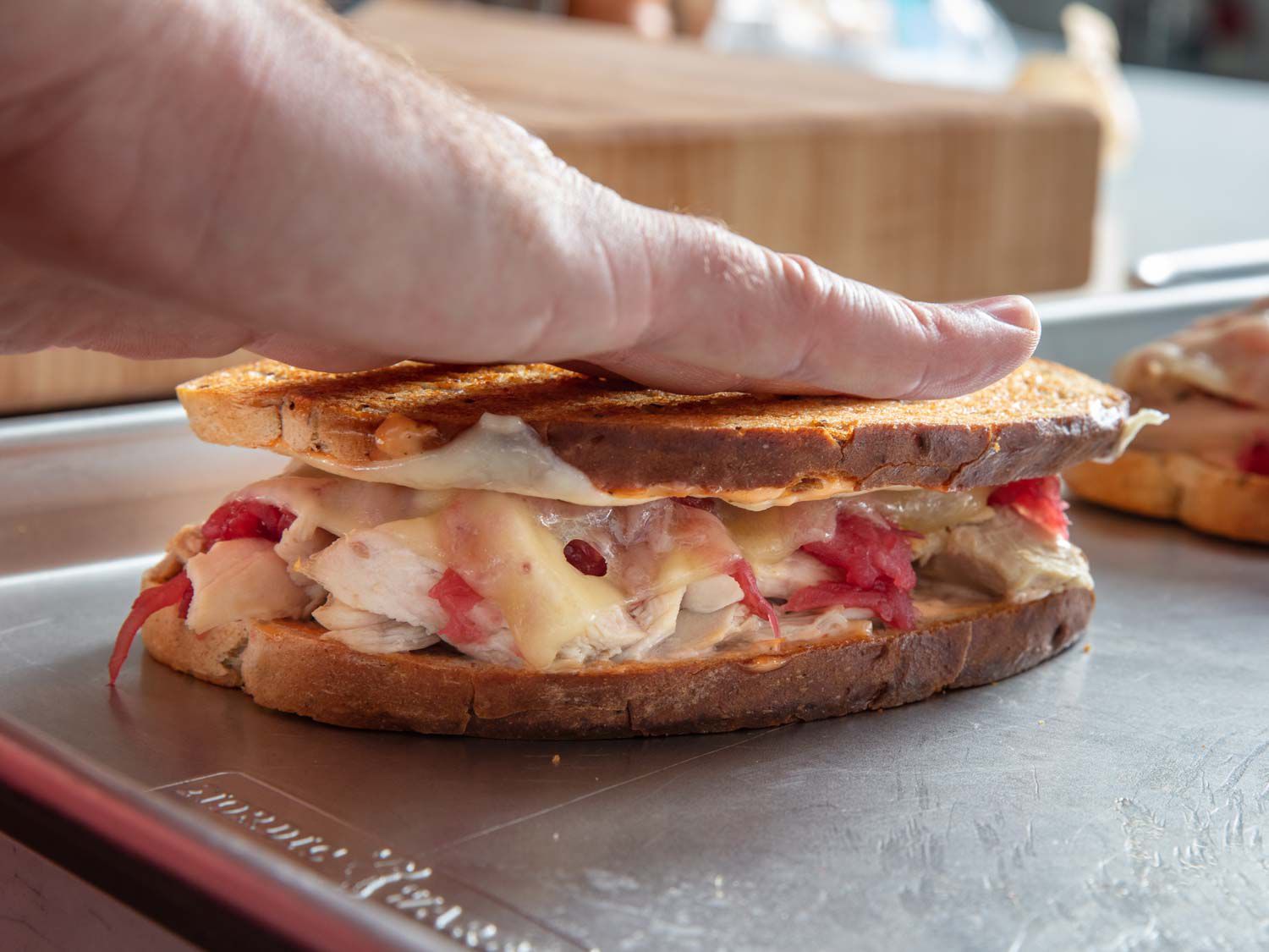 Pressing down on the top slice of a turkey reuben sandwich.