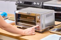 A finger pressing a button on the Breville the Mini Smart Oven BOV450XL