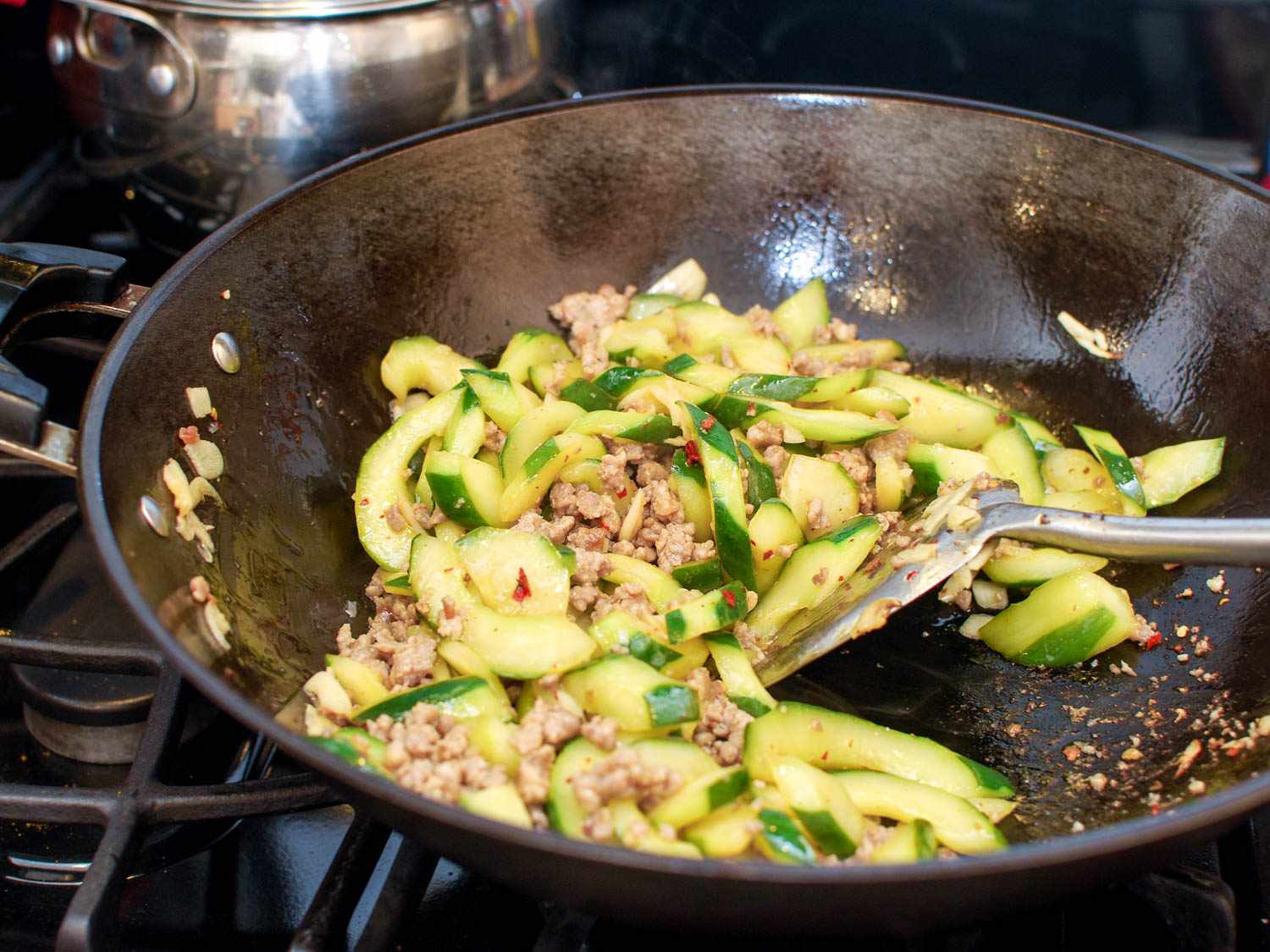 The pork and cucumbers are being stirred together with a wok spatula (or chuan).