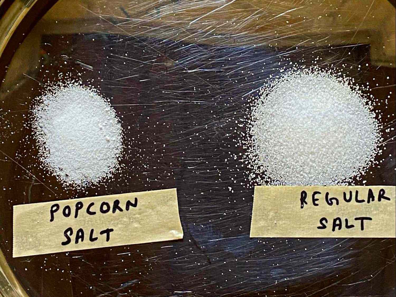 Two types of salt labeled as popcorn salt and regular salt placed on a dark surface