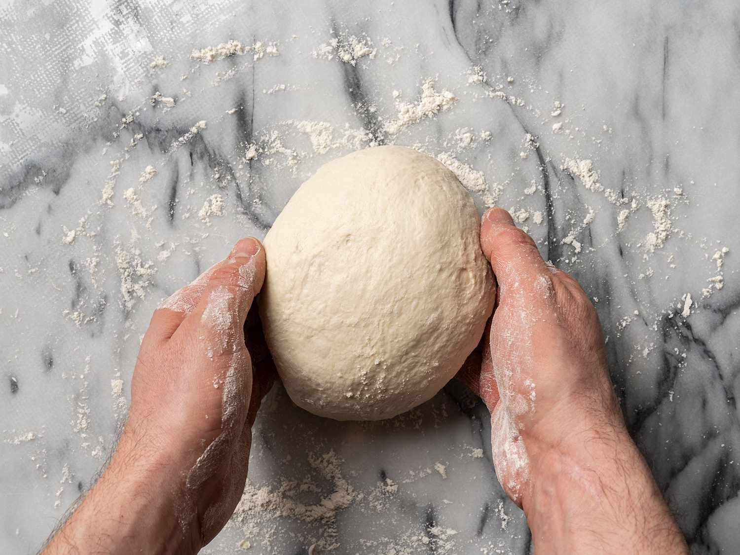 Hands forming a tight ball of focaccia dough