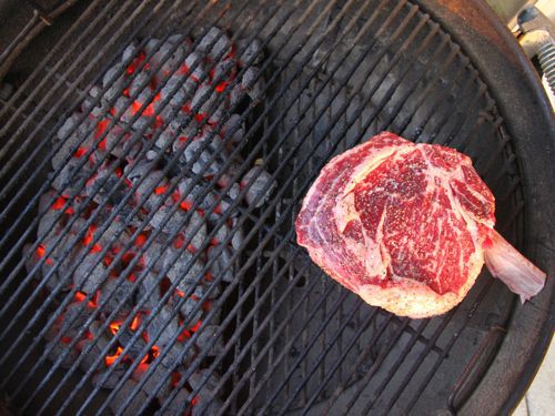 Large marbled steak sitting on grill above glowing pieces of charcoal.