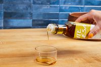 Hand pouring sesame oil into a small clear dish on a wooden countertop