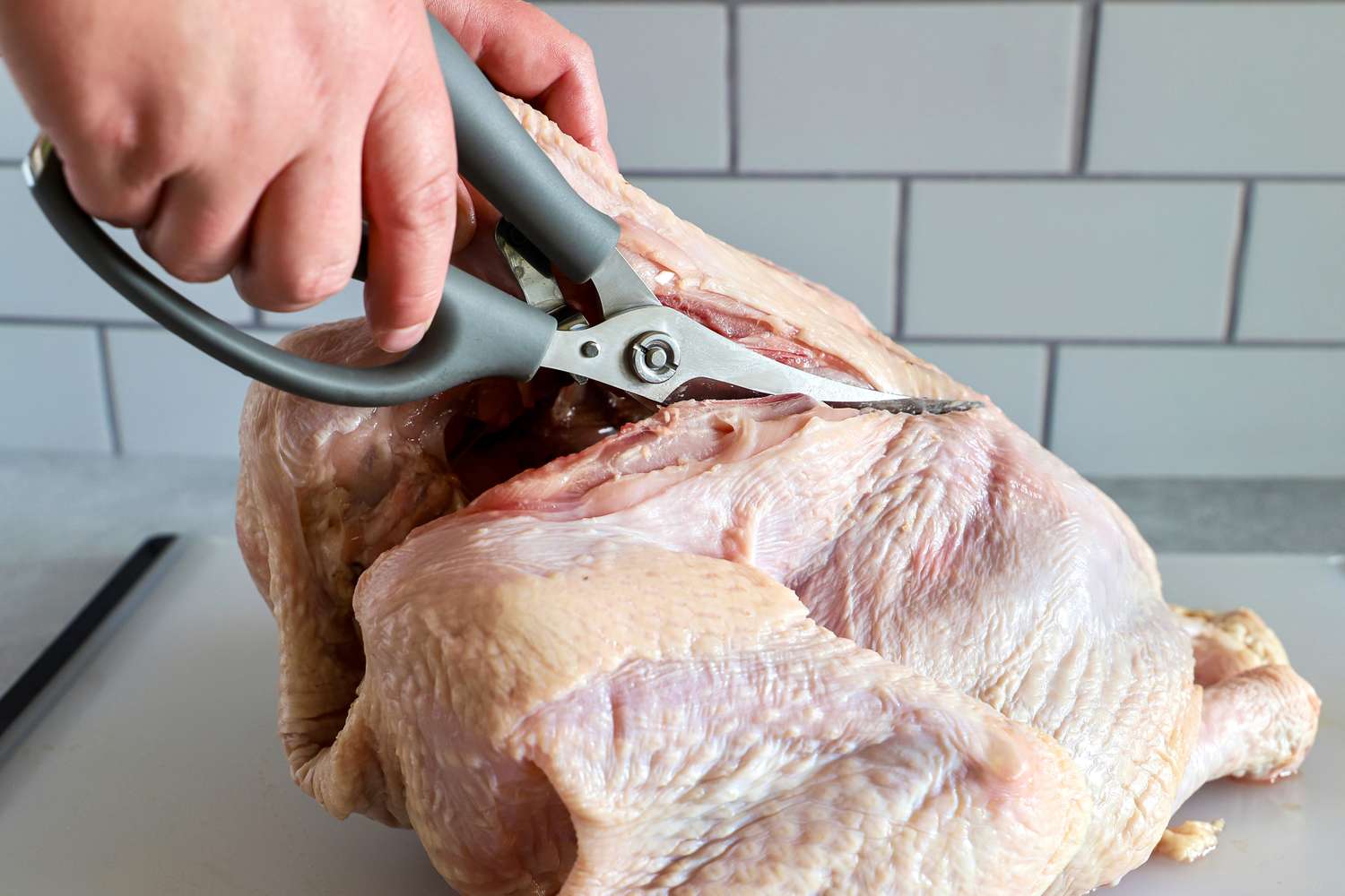 Person using Williams Sonoma poultry shears to cut into a whole raw chicken on a cutting board