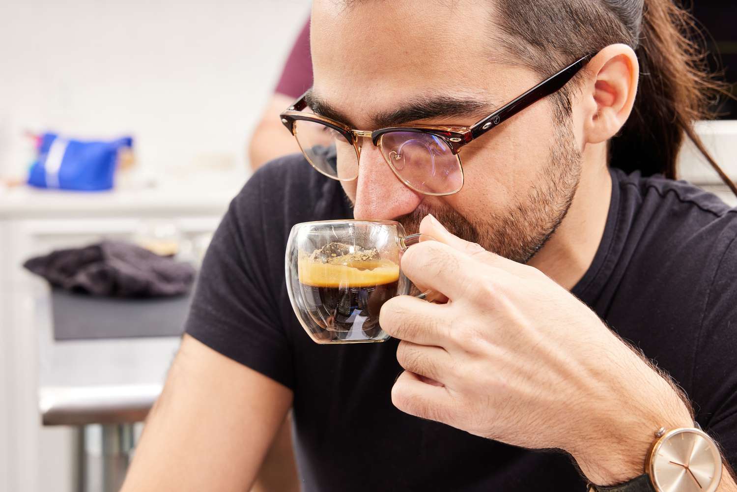 Person holding espresso coffee in a clear mug up to his nose