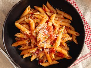A bowl of penne pasta topped with tomato sauce and grated cheese
