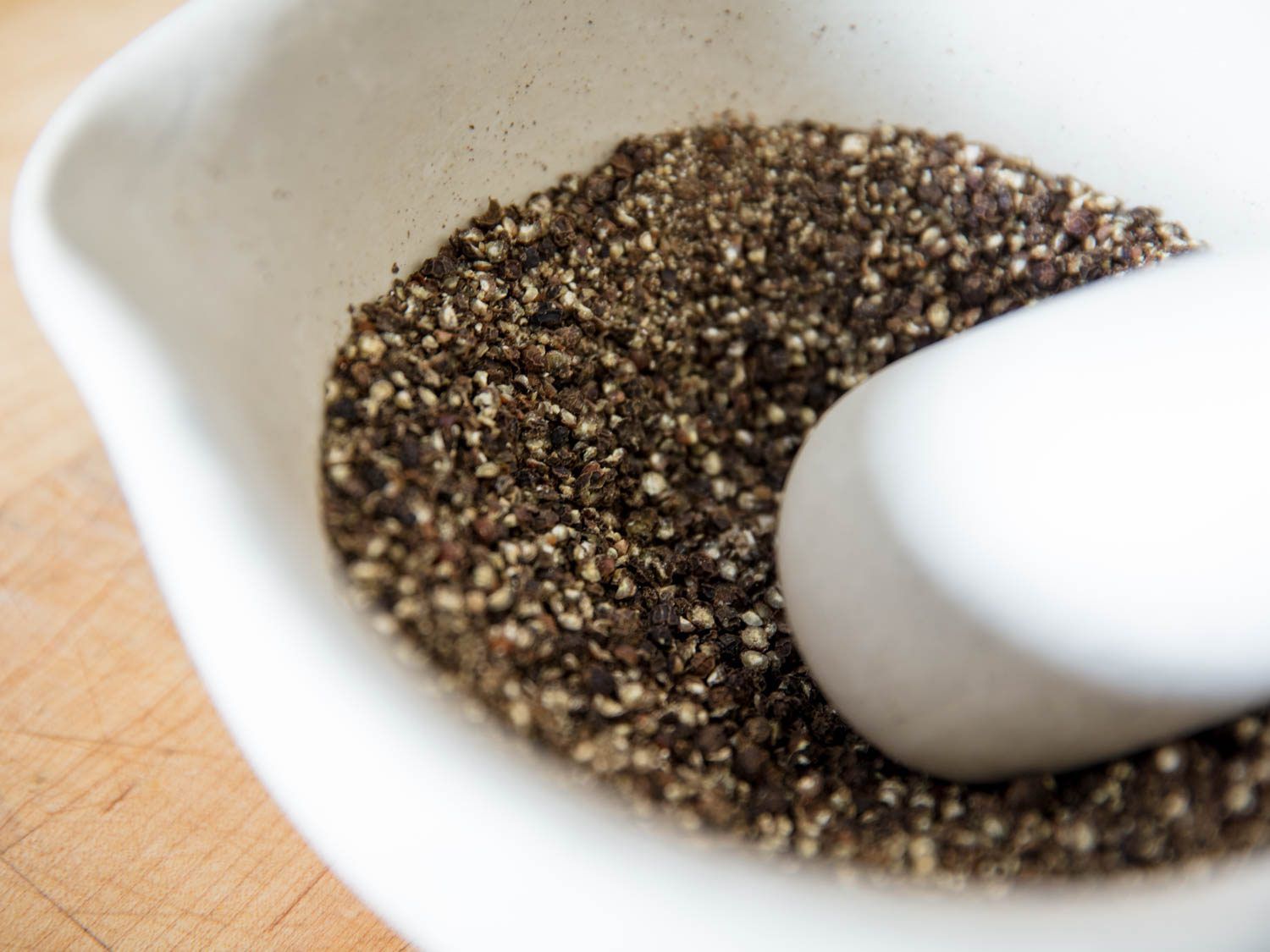 Peppercorns being cracked in a white porcelain mortar with a pestle.