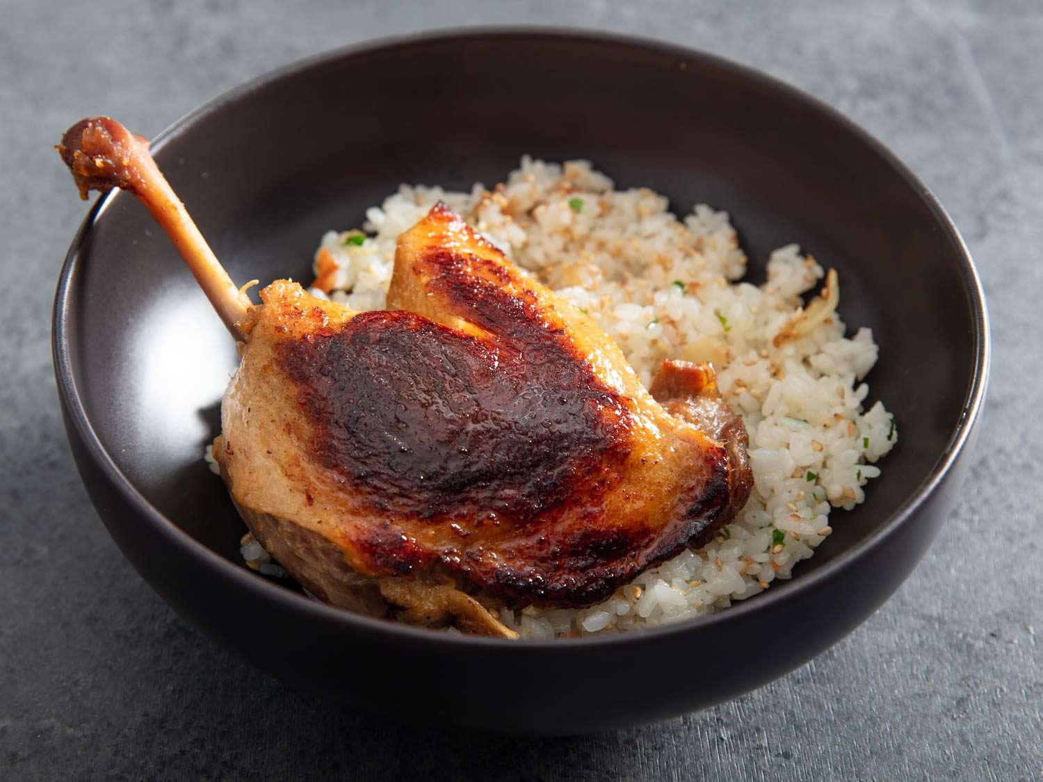 Closeup of a bowl with a crisped leg of koji duck confit over rice.