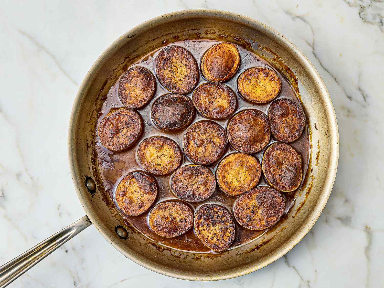 A skillet with layered browned potato slices in a broth