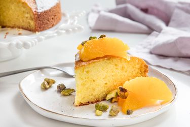 A slice of olive oil cake topped with orange segments and pistachios.
