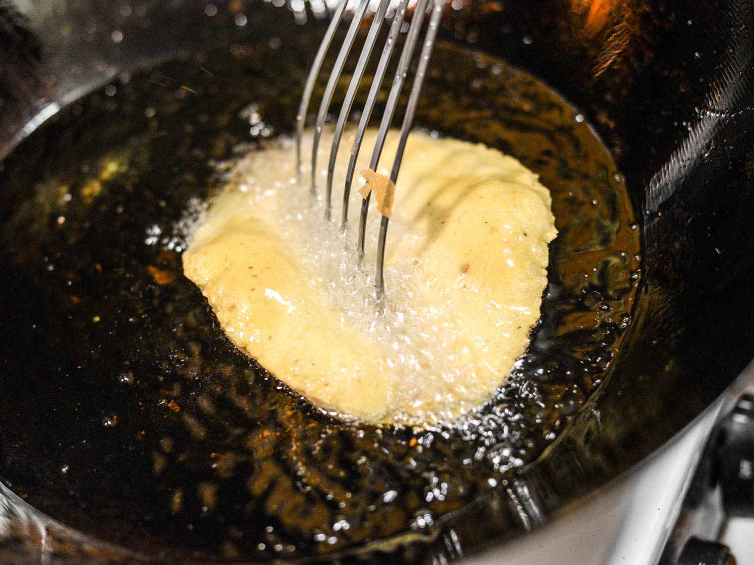 Pressing a deep-frying tortilla with a metal spatula to form a taco shape.