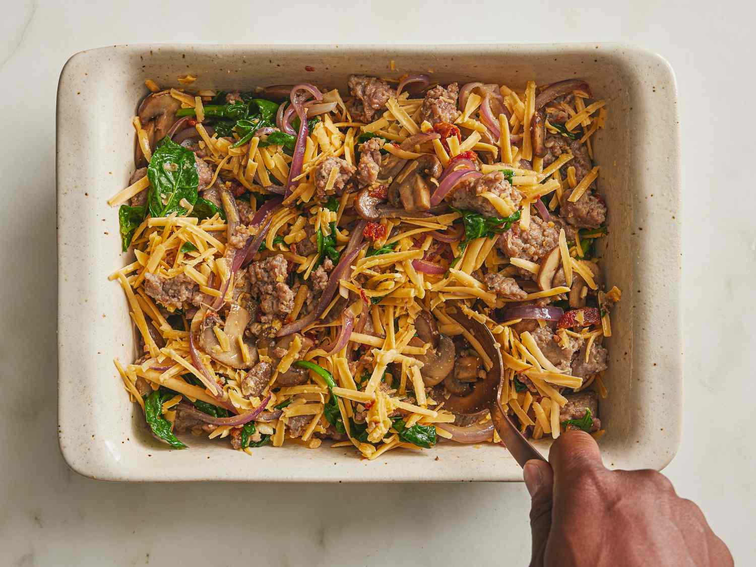 casserole dish with fillings, and shredded cheese being stirred in. 