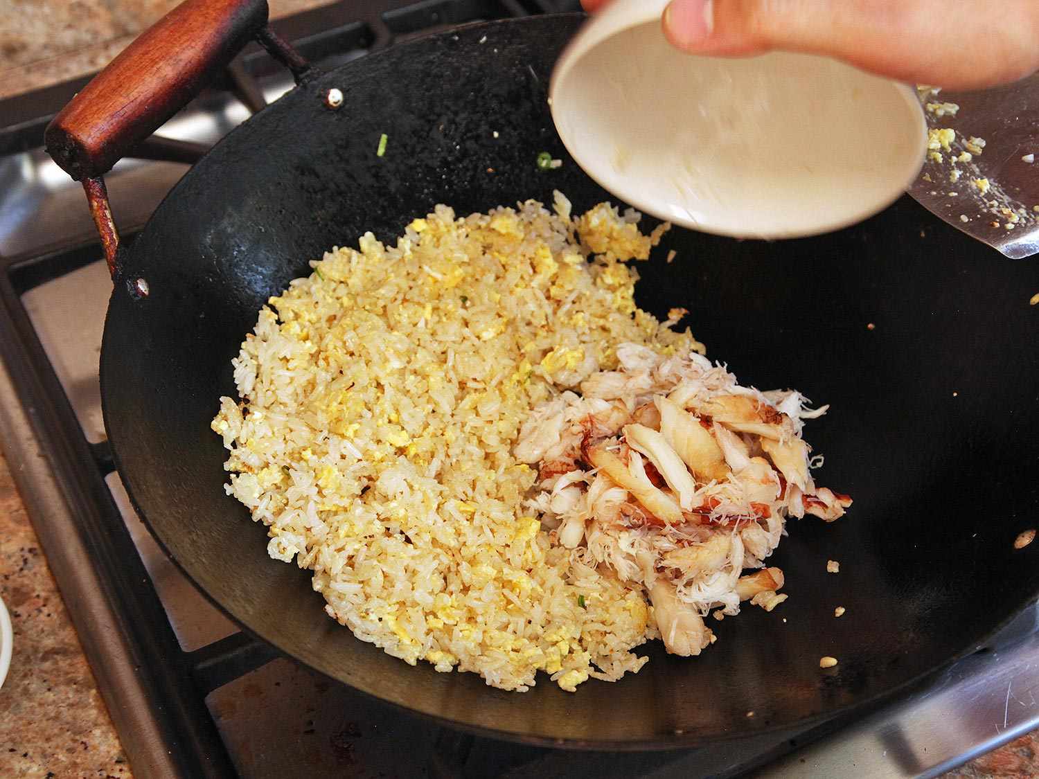 Crab is combined with the fried rice in a wok.
