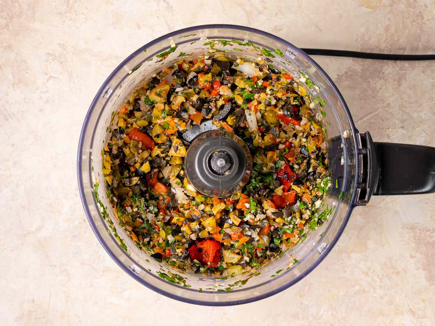 Olives, giardiniera, peppers, parsley, capers, and garlic chopped in the bowl of a food processor.