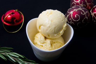 Two scoops of leftover panettone ice cream, served in a small white bowl and surrounded by Christmas tree ornaments and a sprig of basil.