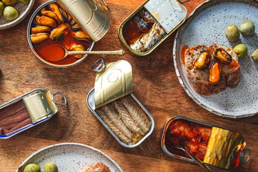 An arrangement of various open tins of fish displayed with accompaniments like olives and bread