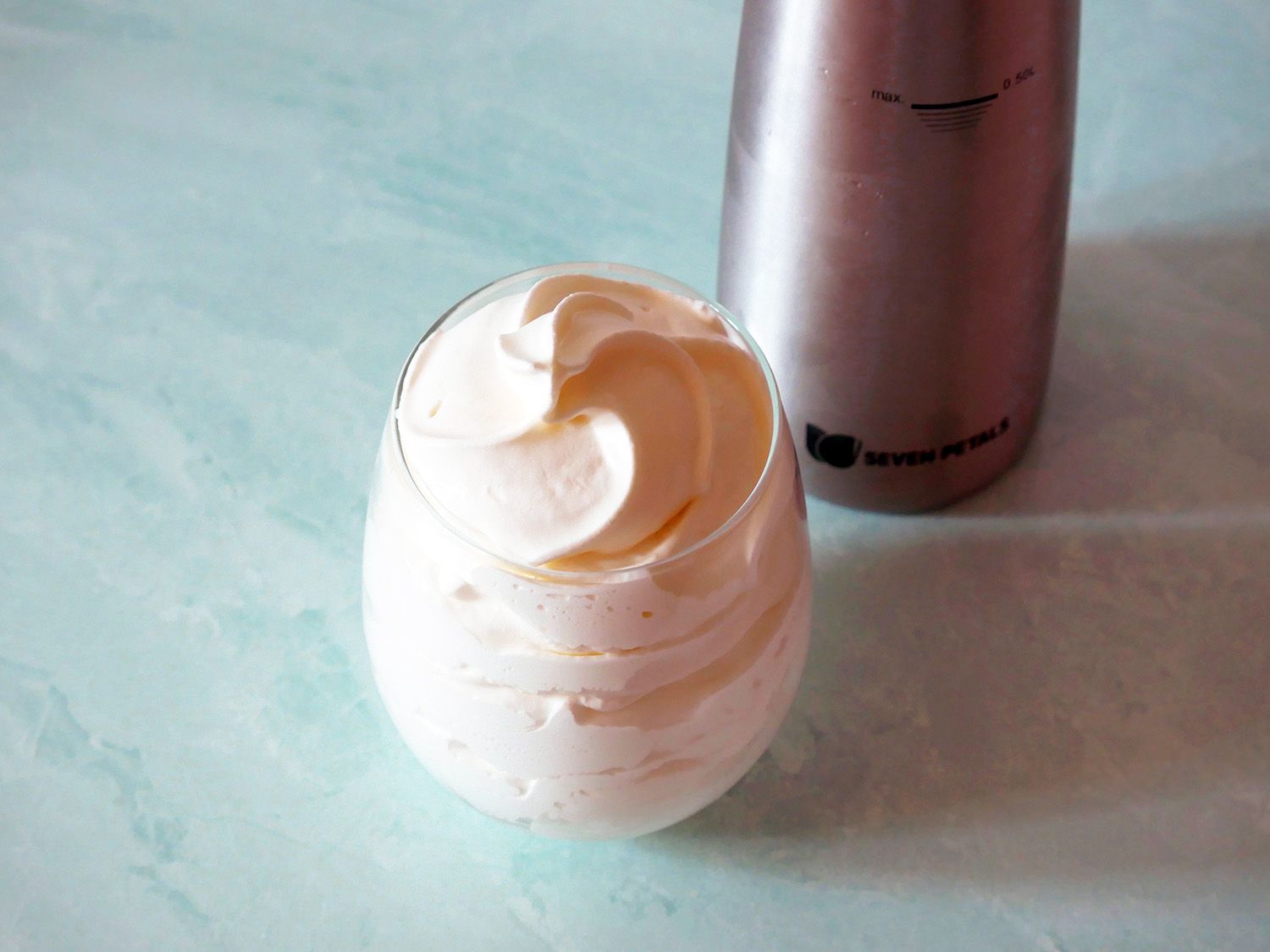 closeup of whipped cream in a glass with the seven petals siphon in the backround