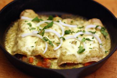 A skillet of enchiladas suizas stuffed with vegetables and topped with sliced onion and cilantro. 