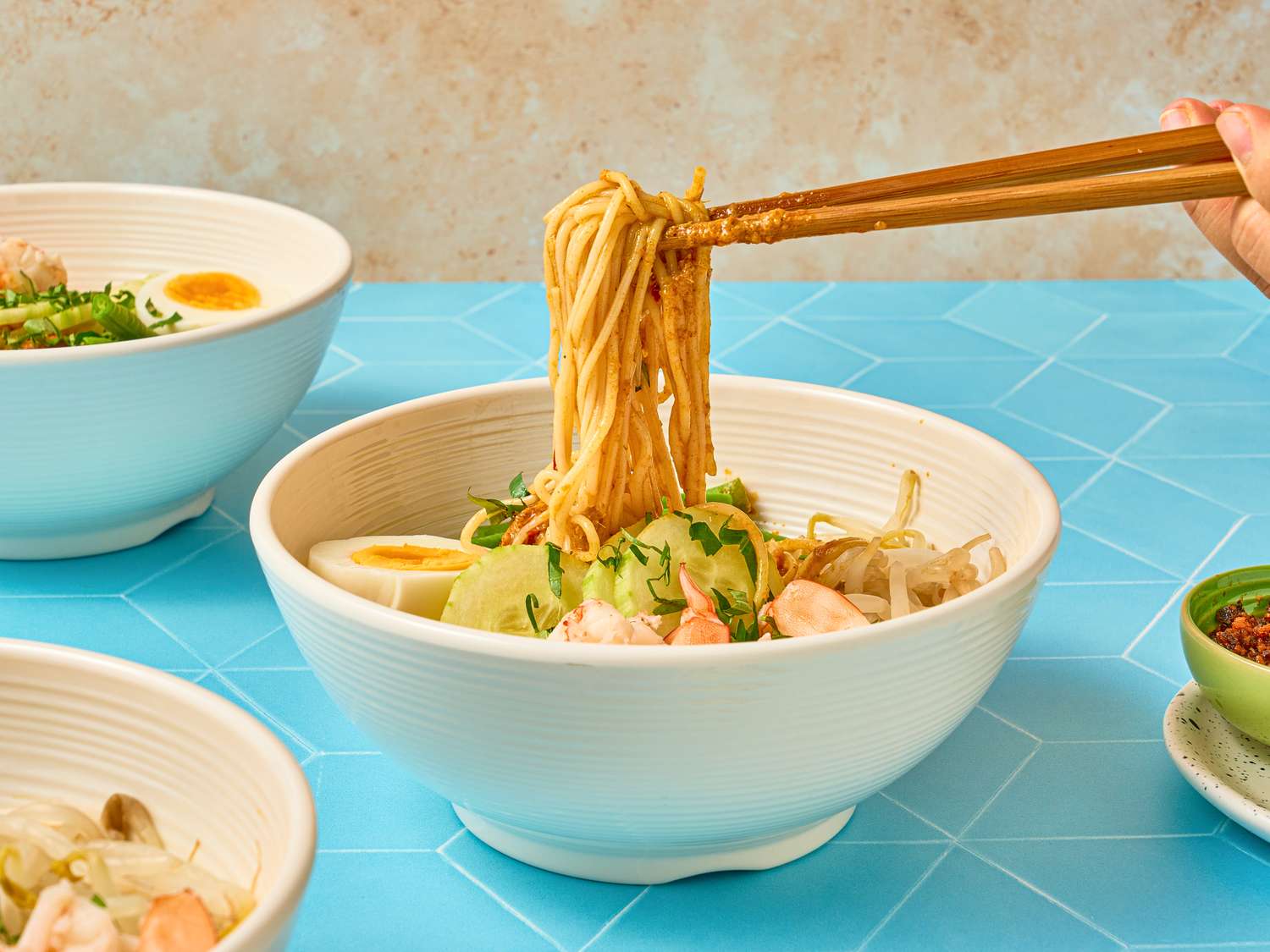 A bowl of curry laksa with noodles lifted by chopsticks surrounded by other dishes on a table