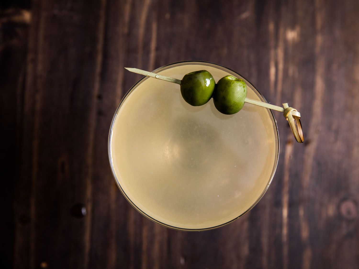 Overhead shot of a mezcal dirty martini with two skewered olive perched on the rim.