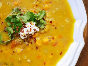 An overhead close-up of bright orange mulligatawny soup garnished with chile flake, fresh cilantro leaves, and a dab of yogurt.
