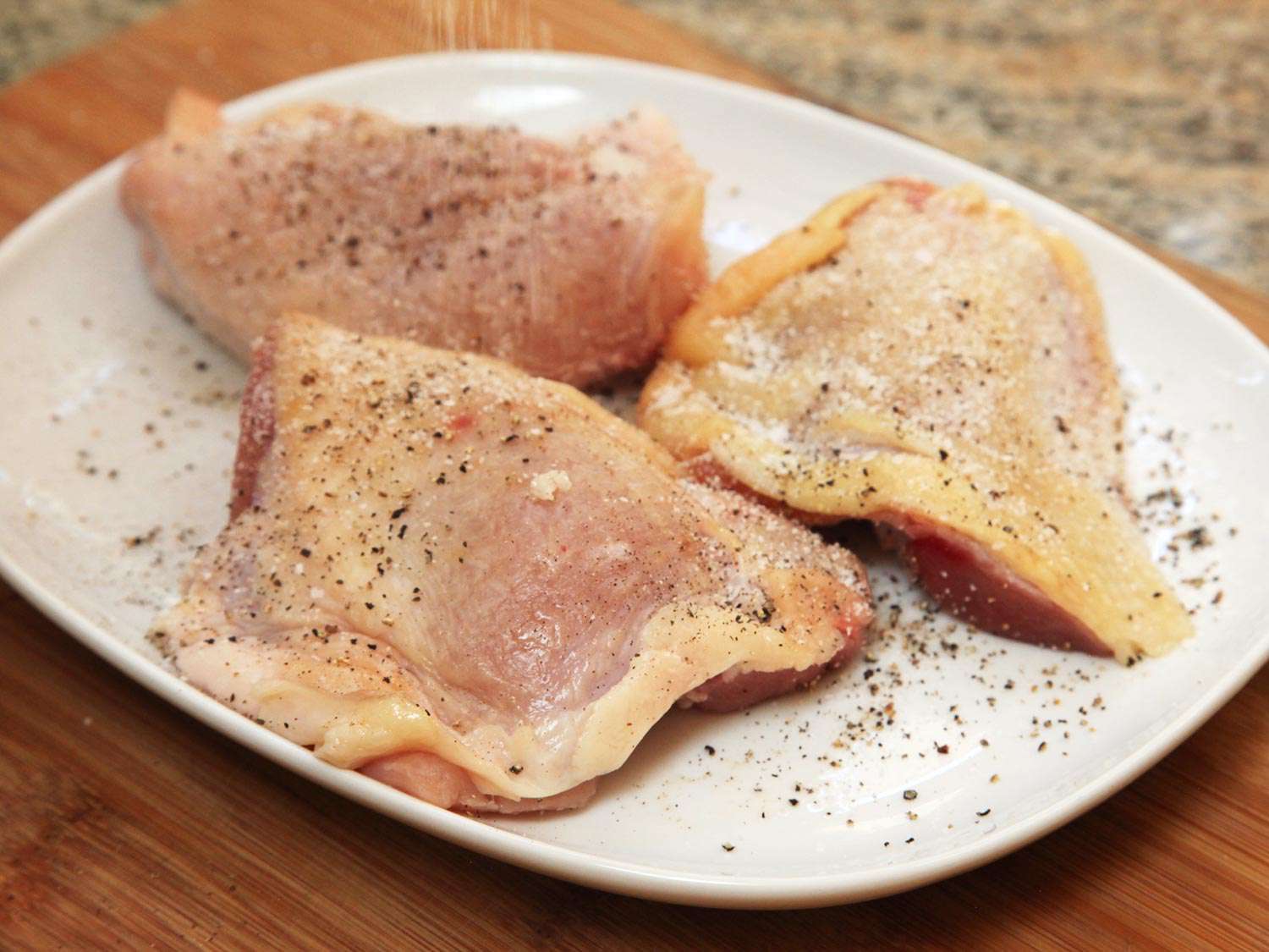 Seasoned raw chicken thighs on a white rectangular plate.