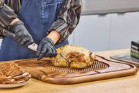 Person carving a roasted chicken on a Lipper International Acacia Cutting Board with Grid Grip