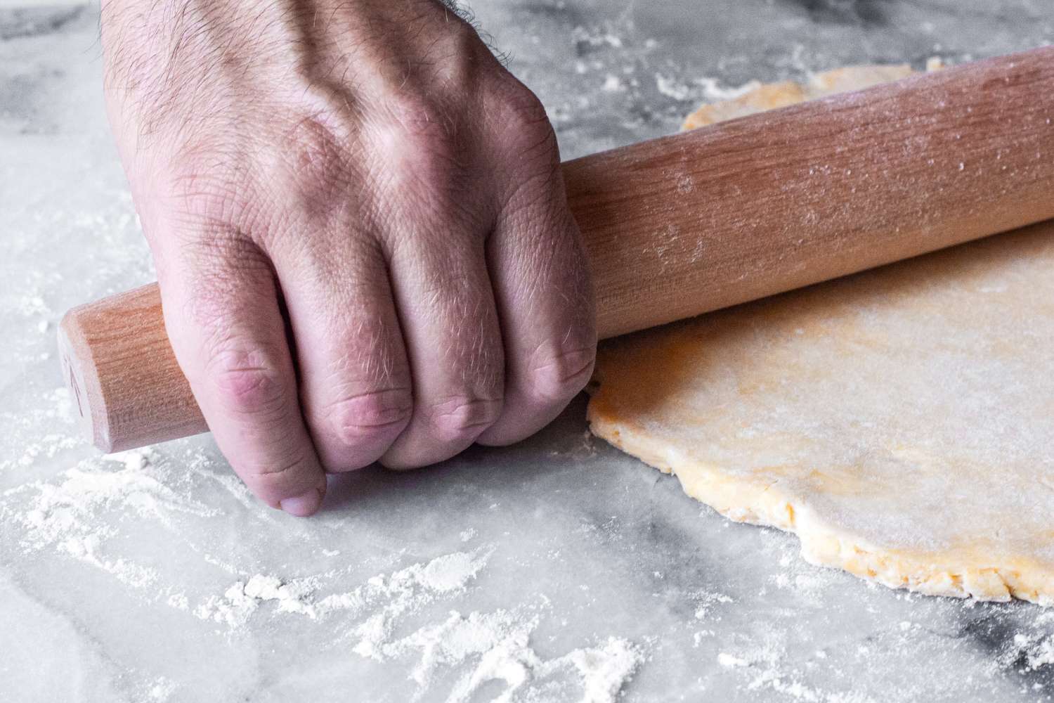 A person rolling out dough with a J.K. Adams Maple French Rolling Pin on a floured surface