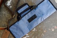 A waterresistantAsaya Chef Knife Roll Bag with handles and a leather strap on a textured surface