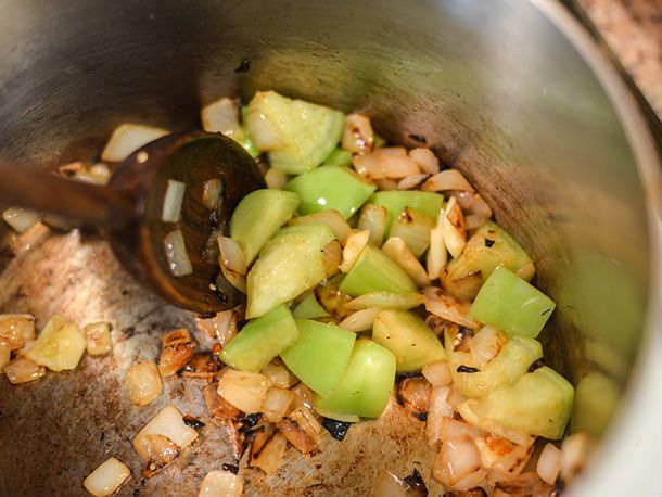 Chopped onions and tomatillo chunks are browned in a saucepan.