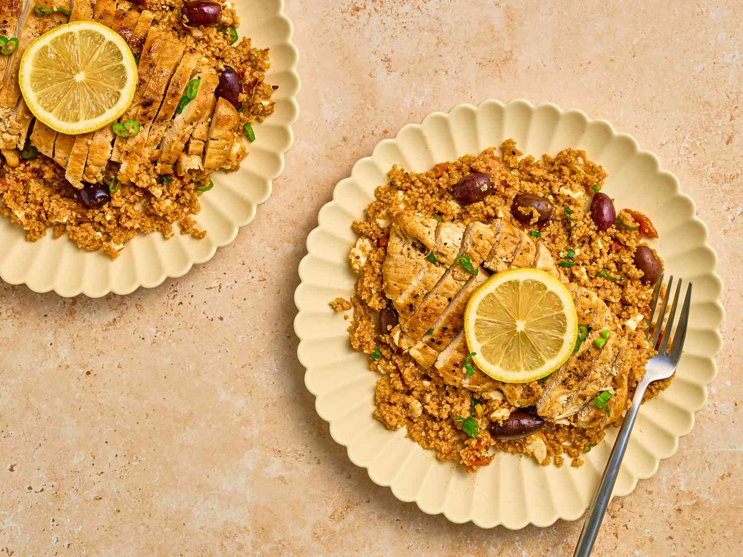 2 pale yellow plates of Chicken with Bulgar pilaf garnished with lemon slices and a fork