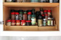 A neatly arranged shelf of spice jars in a kitchen cabinet
