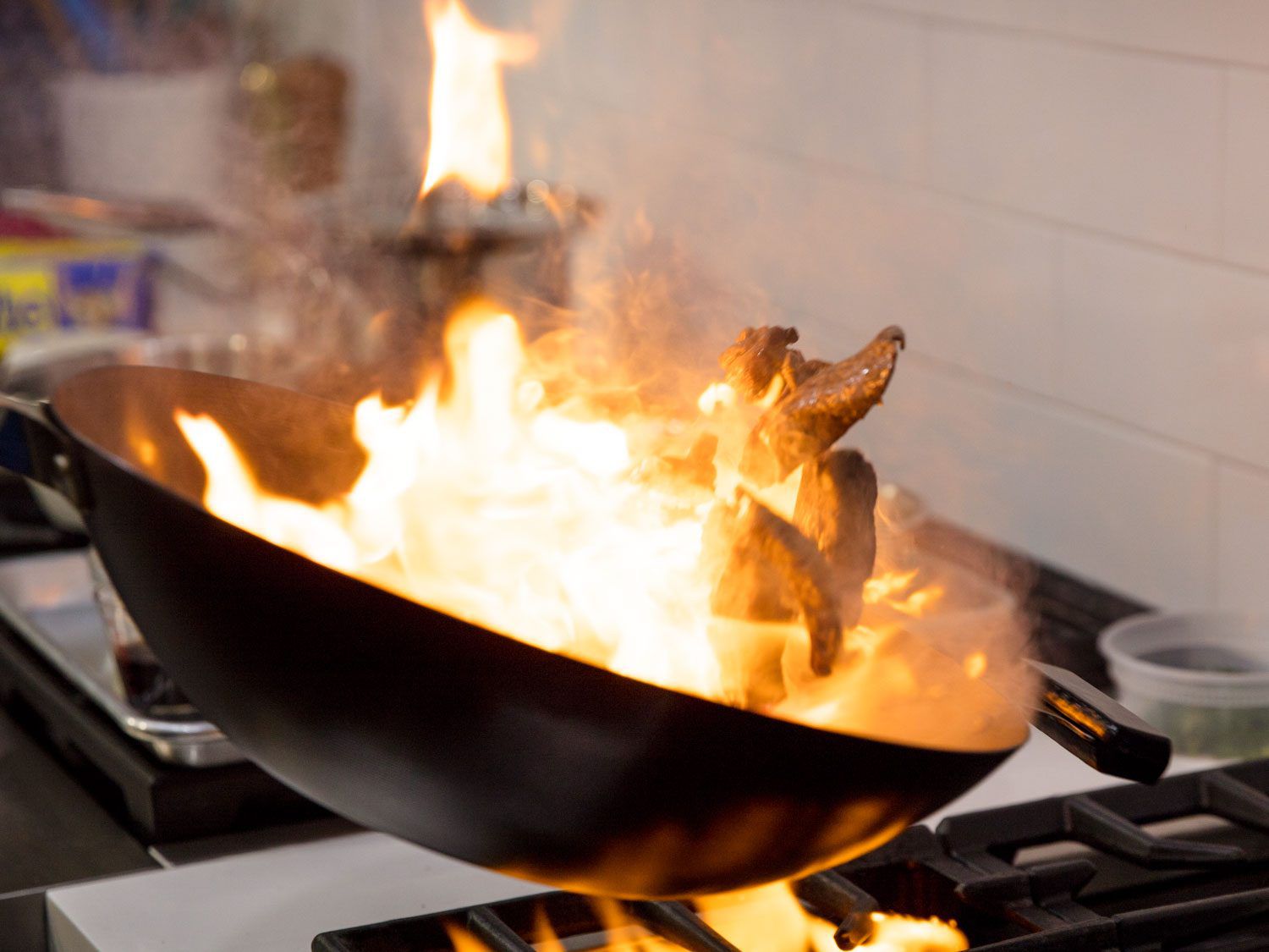 Flames engulf pieces of steak as they are tossed in a wok over high heat.