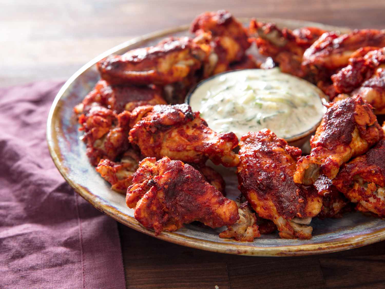 A round plate holding tamarind-ginger glazed chicken wings. In the center of the plate is a small bowl of dipping sauce.