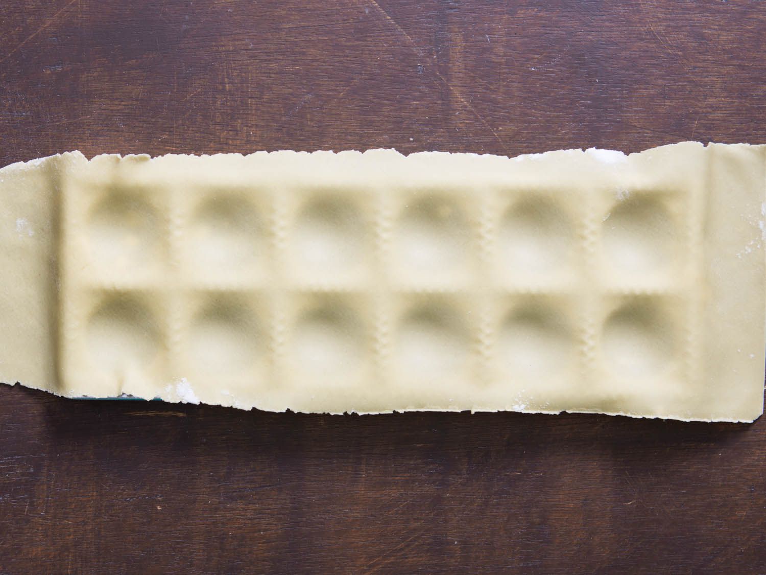 The plastic mold has been removed to reveal the pasta dough in the ravioli mold, with depressions ready to be filled.